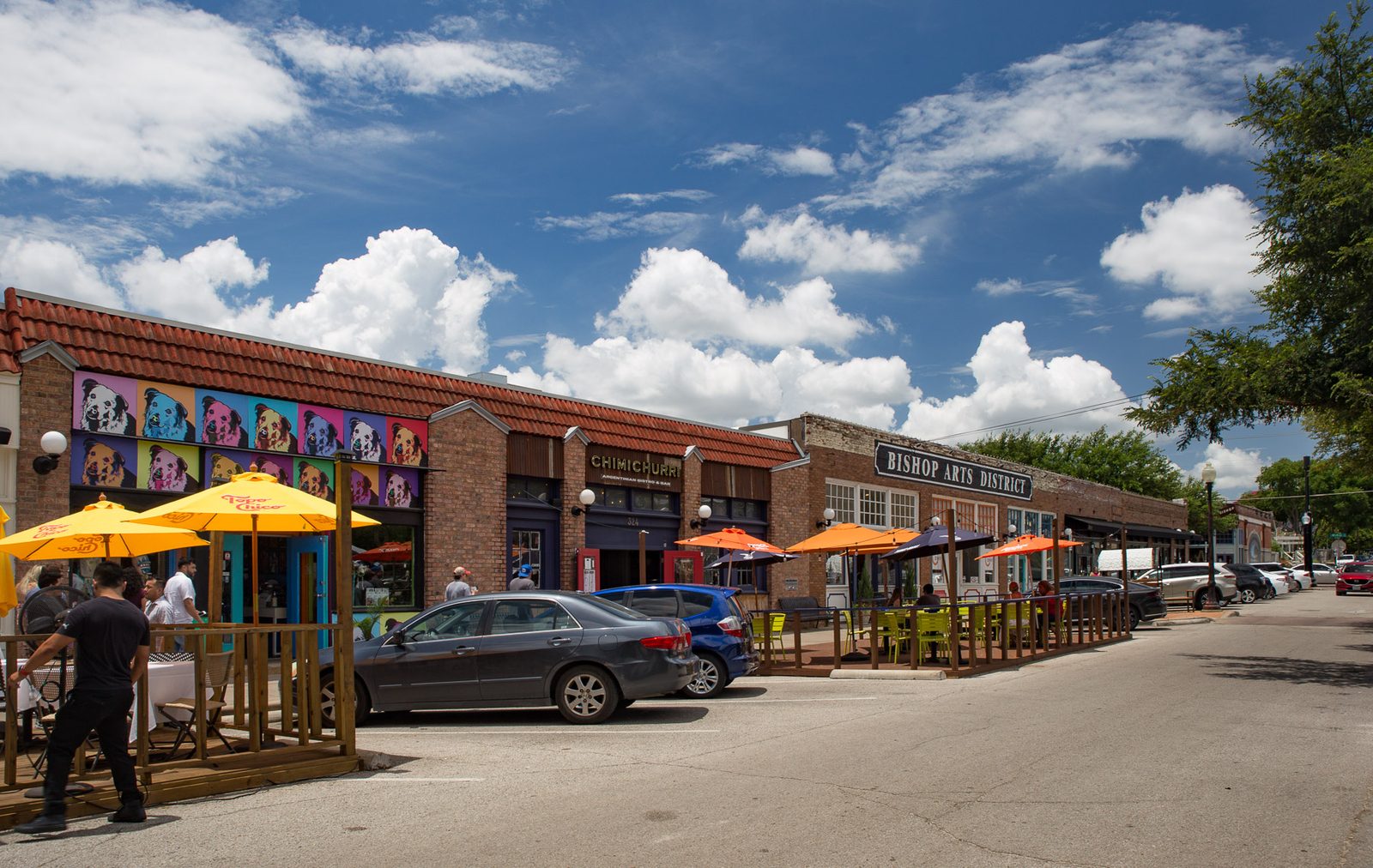 Colorful shopfronts with yellow patio umbrellas along a street in the Bishop Arts District