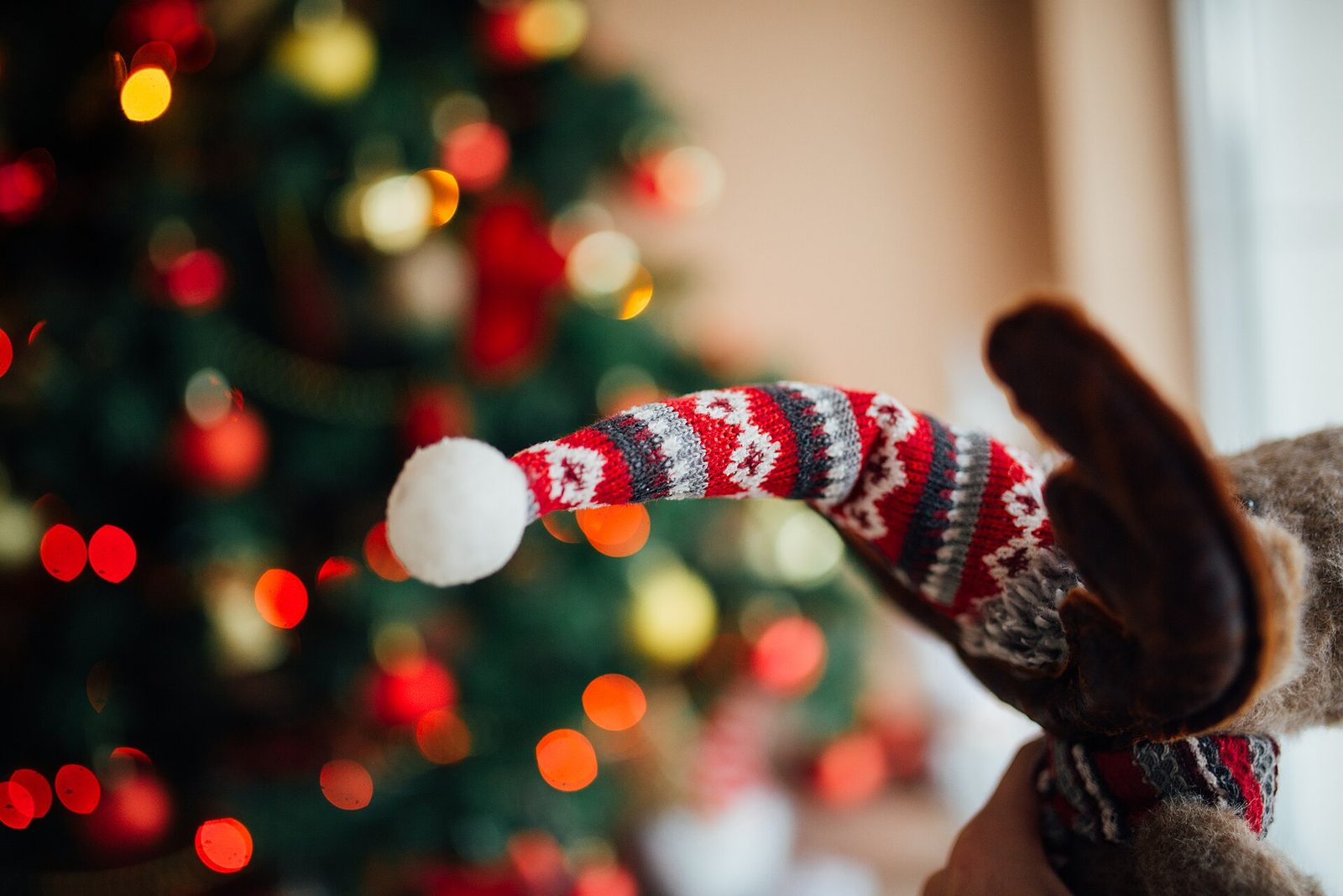 Close-up of a knitted decoration hanging on a Christmas tree with coloured lights behind