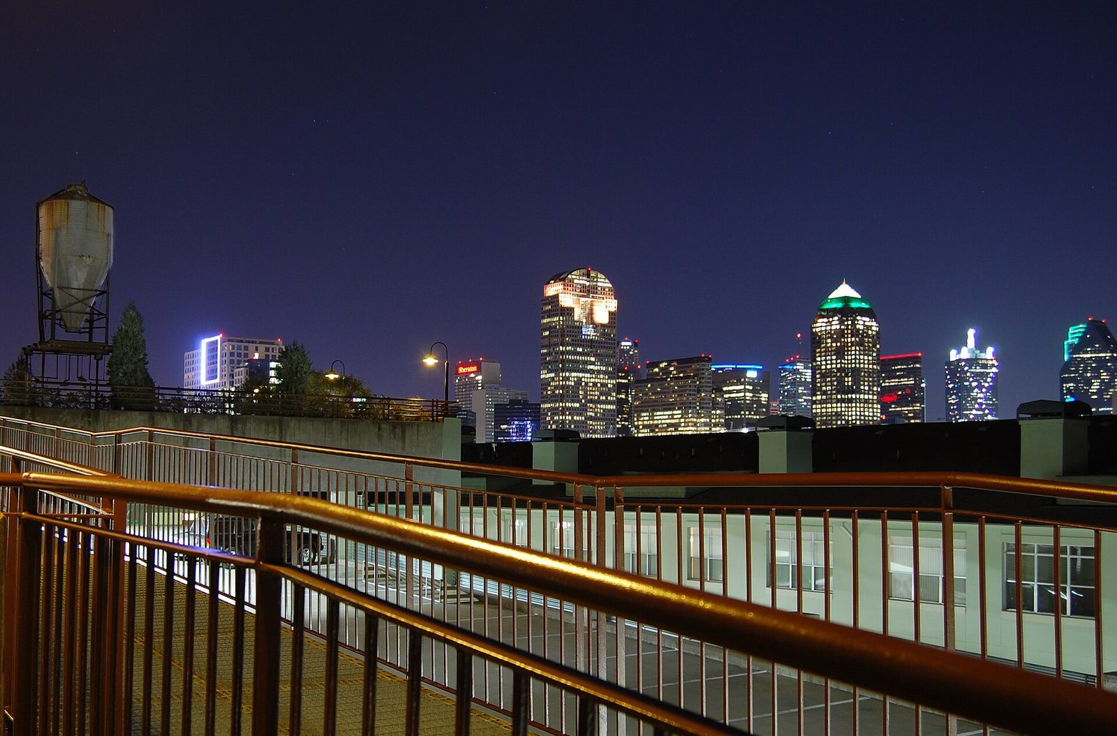The downtown Dallas skyline lit at night seen from a pedestrian railing