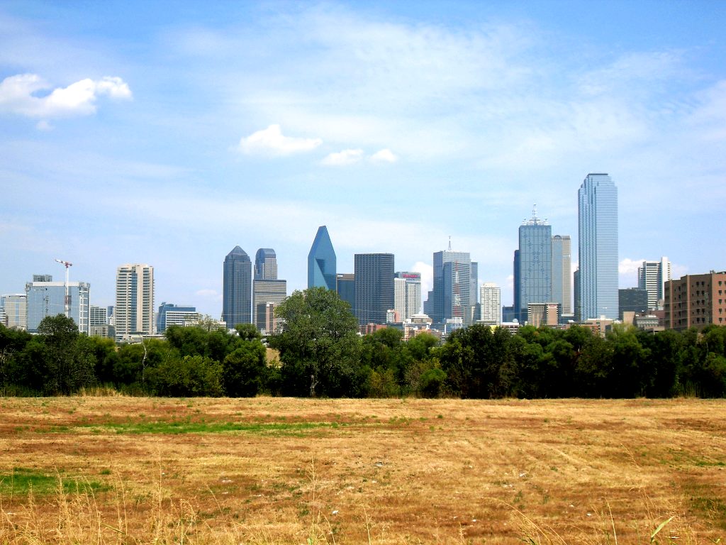 The Dallas skyline seen across a dry winter field under a clear blue sky
