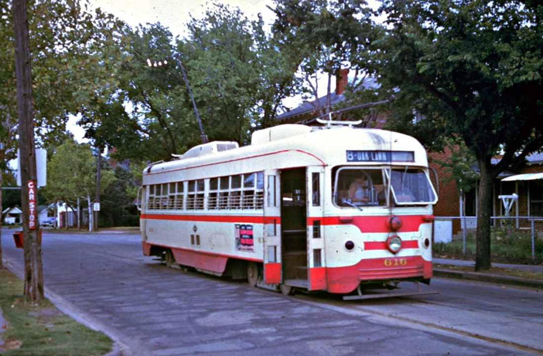 A restored vintage red and white streetcar on a tree-lined Dallas street