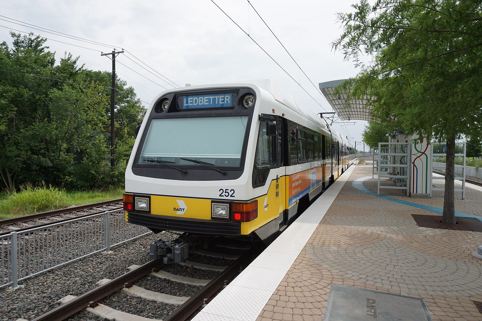 A DART light rail train waiting at an open-air station platform near Dallas