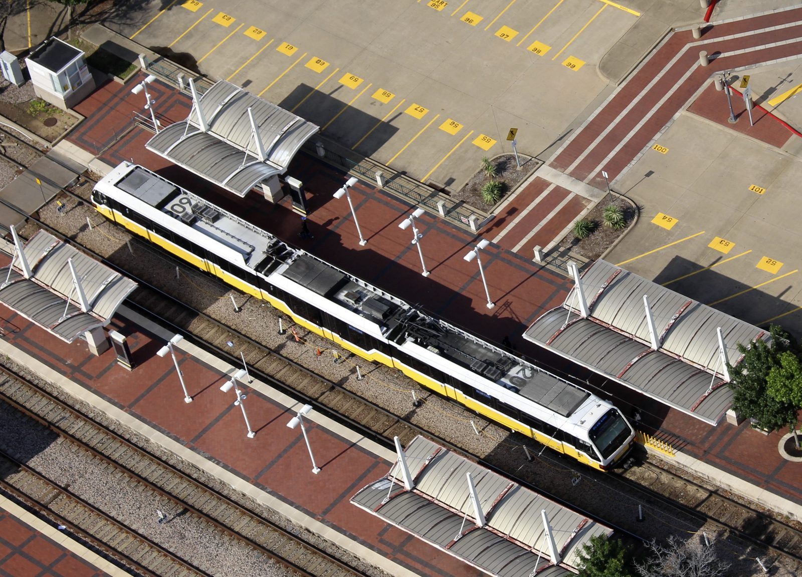An aerial view of a DART light rail train waiting at a station platform in Dallas