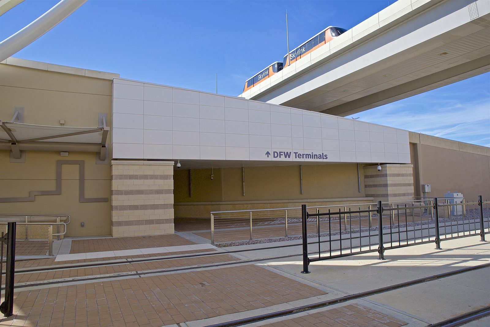 DFW Airport rail station platform with the Skylink people mover track overhead and a sign to the terminals