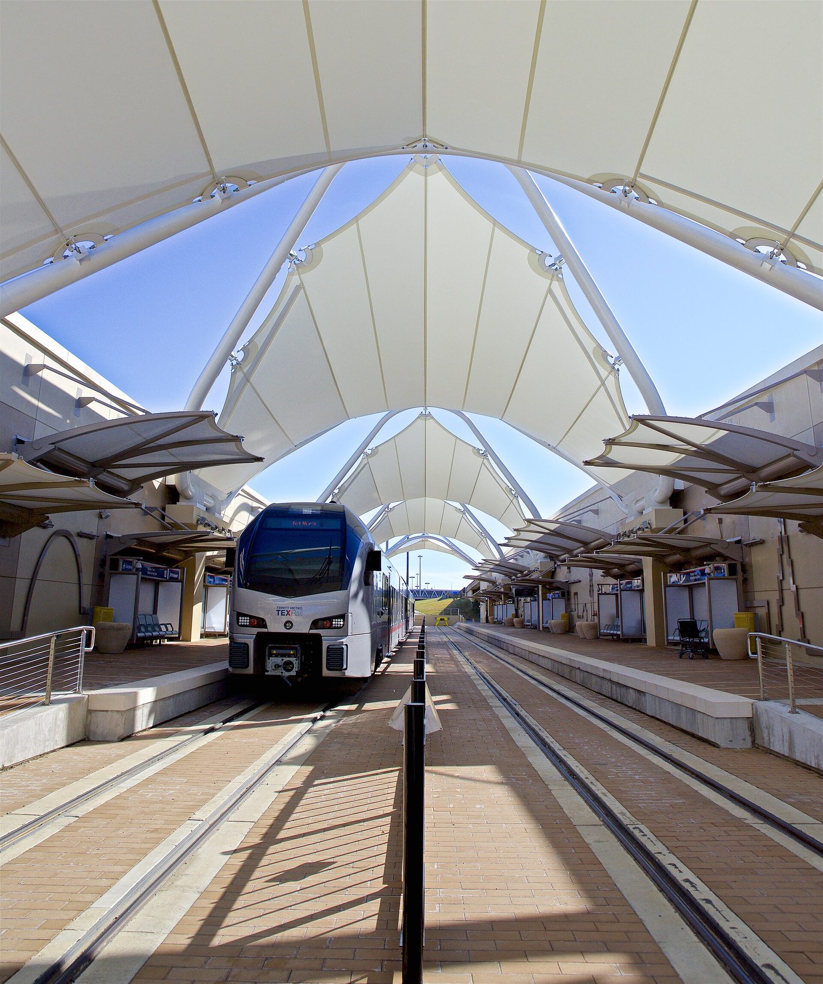 A commuter train at the DFW Airport Terminal B rail station under its curved canopy