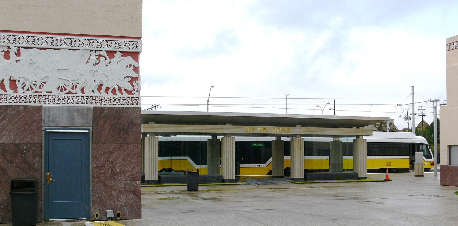 A DART light rail train at Fair Park Station in Dallas beside the art deco building façade