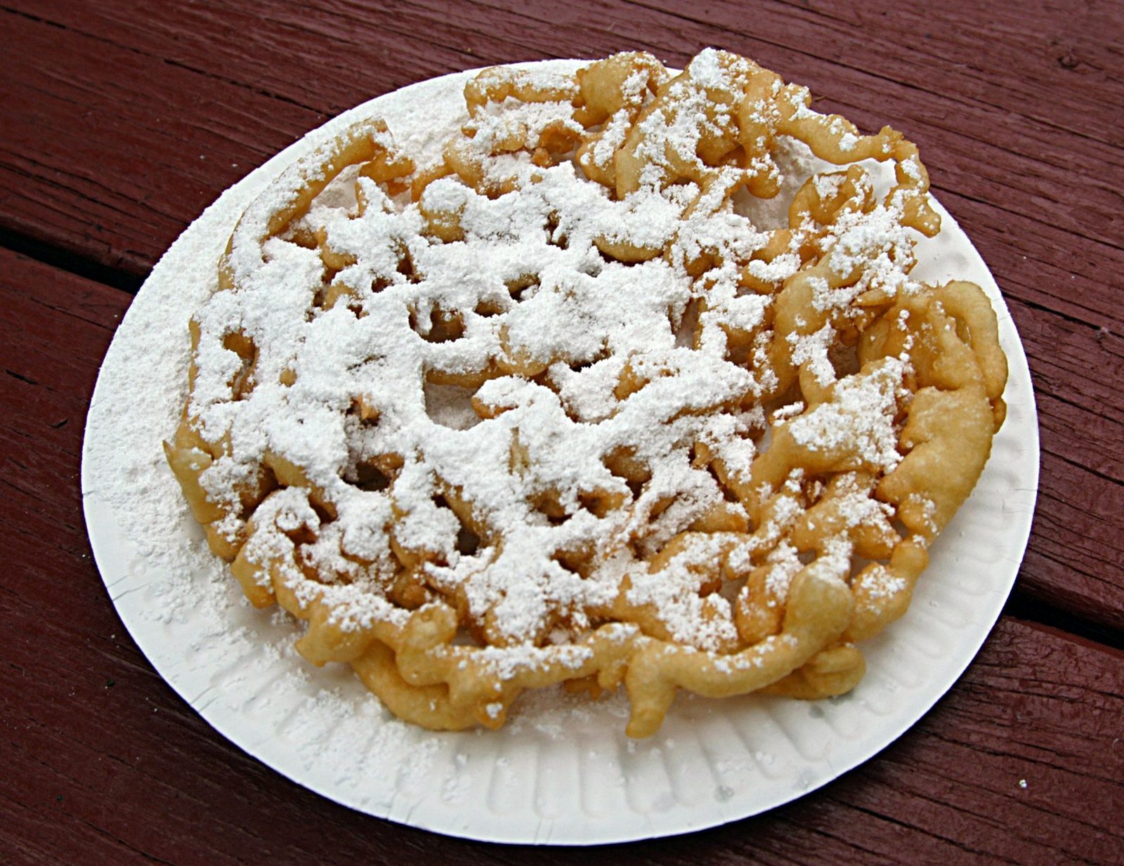 A funnel cake dusted with powdered sugar on a paper plate