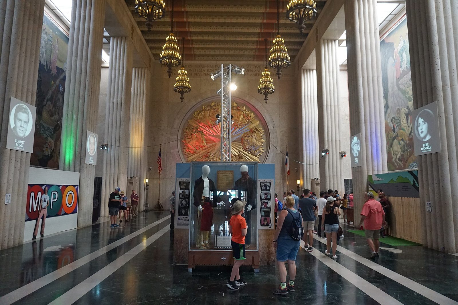 Visitors inside the Hall of State at Fair Park in Dallas, with murals and chandeliers
