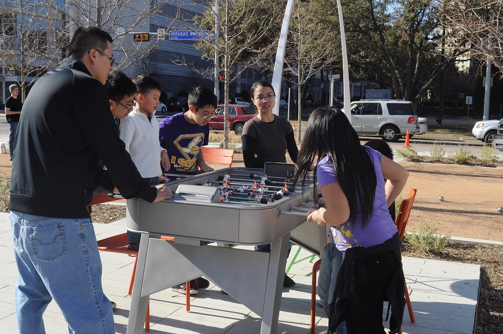 People gathered at outdoor games tables under the trees at Klyde Warren Park in Dallas