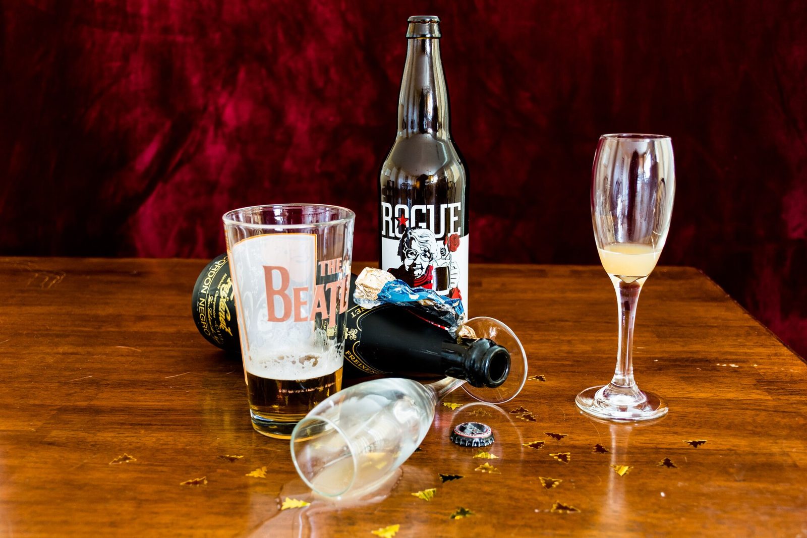 A champagne flute, bottles and scattered confetti on a wooden table after a celebration