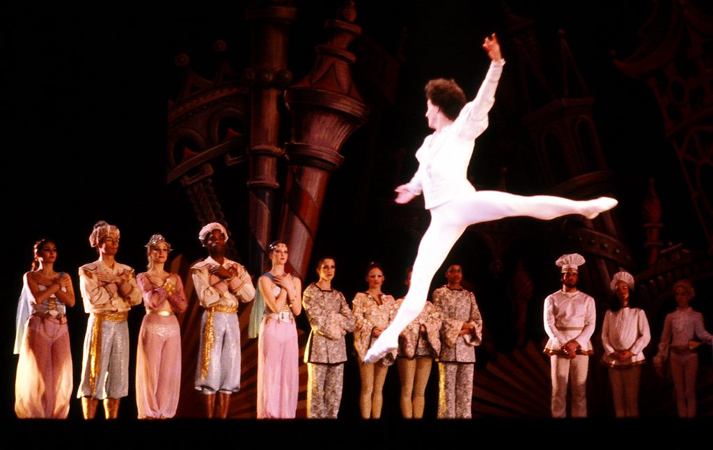 A male ballet dancer mid-leap in front of a line of dancers in a Nutcracker production