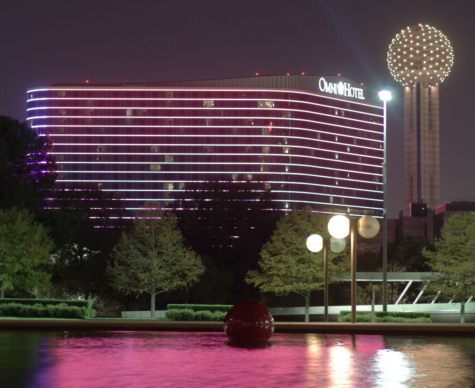 The Omni Dallas Hotel lit up at night beside Reunion Tower with water in the foreground