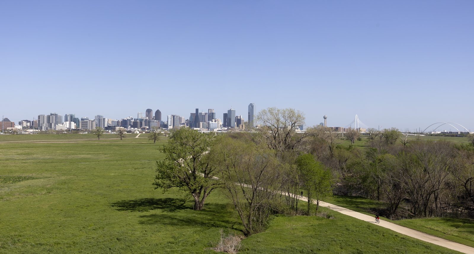Bike and walking trail beside the Trinity River with the Dallas skyline in the distance, a dog friendly Dallas route with open grass